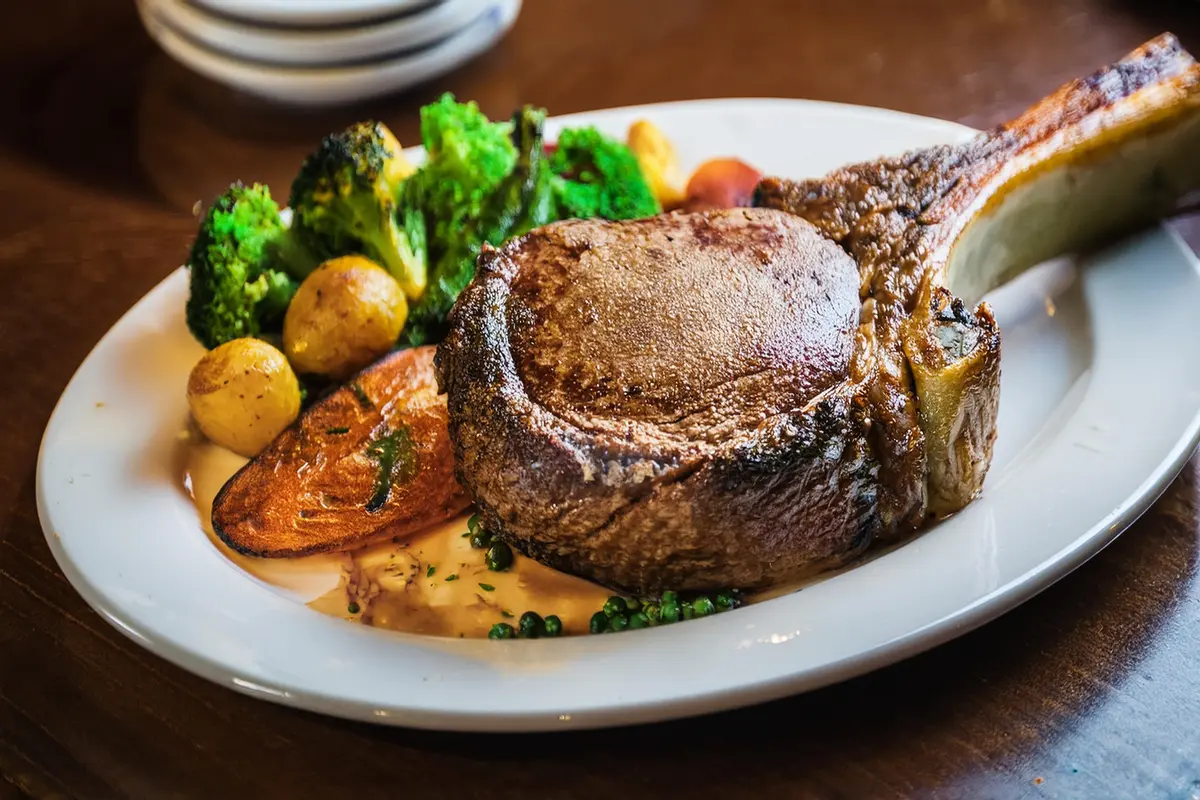 Perfectly grilled tomahawk steak with a long bone, served on a wooden cutting board with rosemary and garlic cloves.